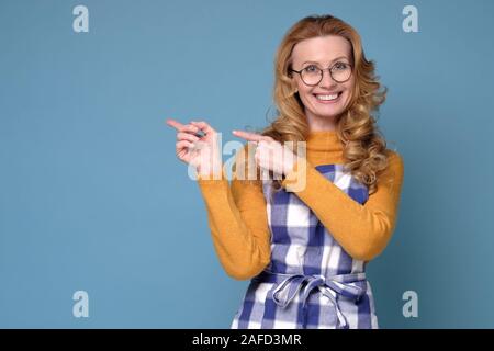 Frau mit Schürze lächelnd und mit Blick auf die Kamera zeigte mit zwei Händen Stockfoto