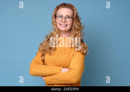 Attraktives Lächeln, elegante Frau mit langen Haaren und Brille mit gefalteten Händen Stockfoto