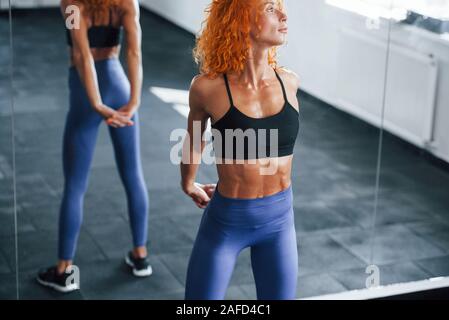 Warm up Übungen. Sportliche rothaarige Mädchen haben fitness Tag in der Turnhalle am Tag. Muskulöse Körper Typ Stockfoto