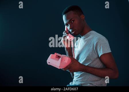 Retro pink Handy. Futuristische Neon Beleuchtung. Junge afrikanische amerikanische Mann im Studio Stockfoto