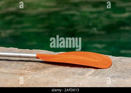 Detail einer orange Paddel für Kajak auf dem Kai des Hafens mit grünem Wasser in der Hintergrund verschwommen Stockfoto