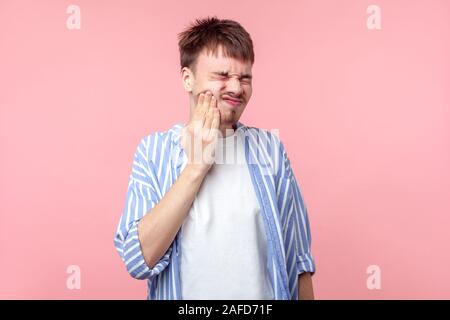 Porträt der kranke junge braunhaarige Mann mit dem kleinen Bart und Schnurrbart in casual Shirt leiden schreckliche Zahnschmerzen, berühren die Wange und schließen die Augen fr Stockfoto