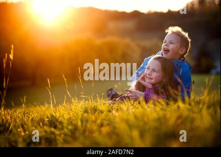 Geschwister sitzen bei Sonnenuntergang auf einer Wiese Stockfoto