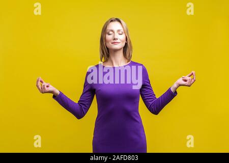 Yoga Praxis, Harmonie. Portrait von friedlichen Frau in lila Kleid Stehen mit geschlossenen Augen und ruhige Gesicht zu meditieren, die Finger in Mudra gestur Stockfoto