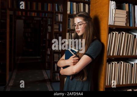 Hält viele Bücher in die Hände. Studentin ist in der Bibliothek. Konzeption von Bildung Stockfoto