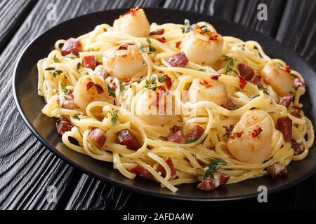Portion Spaghetti mit Jakobsmuscheln und Speck in einer cremigen Käse Sauce mit Kräutern close-up in einem Teller auf dem Tisch. Horizontale Stockfoto