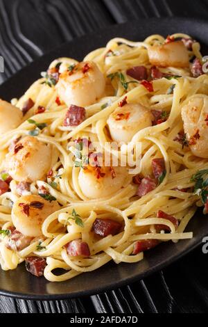Italienische Spaghetti mit Jakobsmuscheln und Speck in einer cremigen Käse Sauce close-up in einem Teller auf dem Tisch. Vertikale Stockfoto