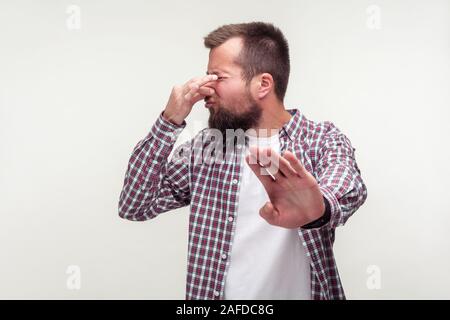 Portrait von verwirrt bärtiger Mann im casual Plaid Shirt, stop Geste und kneifen Nase mit Ekel Grimasse, Gefühl der Abscheu zu unangenehmen sm Stockfoto