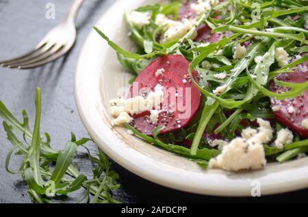 Ton Teller mit Rote Bete RUCOLA UND FETA-Käse Salat auf Schiefer fach Detailansicht. Gabel zur Seite Stockfoto