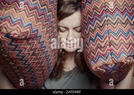 Woman close ears with pillows. Stressed woman having headache or migraine. Negative emotions concept Stockfoto