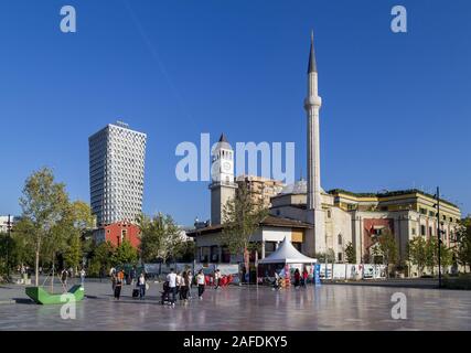 Der Hauptplatz von TiranaThe Et'Hem Bey Moschee, der Osmanischen Uhrturm, die modernen Hotels, die Nationalflagge und die Reiterstatue von skenderbeg Stockfoto