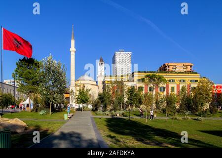 Der Hauptplatz von TiranaThe Et'Hem Bey Moschee, der Osmanischen Uhrturm, die modernen Hotels, die Nationalflagge und die Reiterstatue von skenderbeg Stockfoto