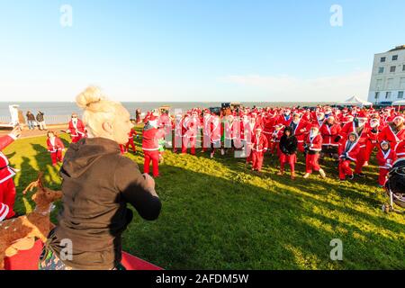 Eine große Gruppe von Menschen, die sich alle als Pater Xmas verkleidet haben, versammelte sich an der Küste von Margate für den jährlichen Pilgerhospiz-Spaßlauf "Santa am Strand". Gruppe, die während einer Gruppenübung den Anweisungen eines vor ihnen befindlichen Fitnesstrainers folgt. Stockfoto