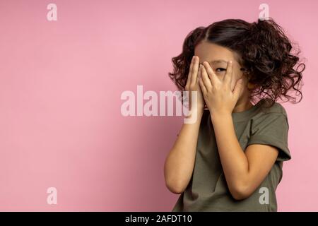 Terrified asiatische Mädchen mit lockigem Haar, in Khaki t-shirt, das Gesicht mit beiden Handflächen, verstecken, spähen durch die Finger, furchtsam, Cartoon, isolat Stockfoto