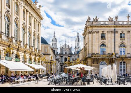 Straßencafé des Grand Hotels auf dem Stanislas-Platz in Nancy, Frankreich, geschlossen durch ein vergoldetes schmiedeeisernes Tor mit der Kathedrale von Nancy im Hintergrund Stockfoto