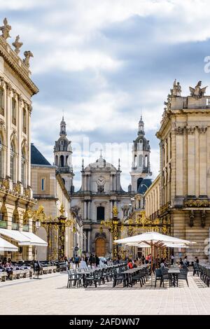 Straßencafé des Grand Hotels auf dem Stanislas-Platz in Nancy, Frankreich, geschlossen durch ein vergoldetes schmiedeeisernes Tor mit der Kathedrale von Nancy im Hintergrund Stockfoto