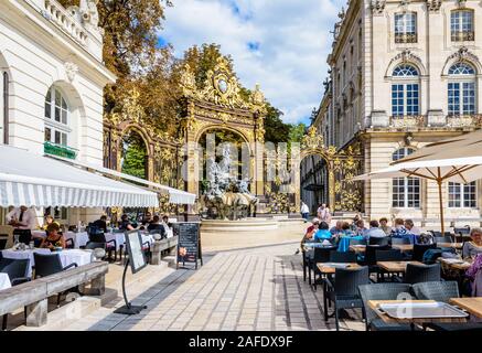 Sonniges Mittagessen in einem Straßenrestaurant auf dem Stanislas-Platz in Nancy, Frankreich, und der Brunnen von Amphitrite und sein vergoldetes Tor im Hintergrund Stockfoto