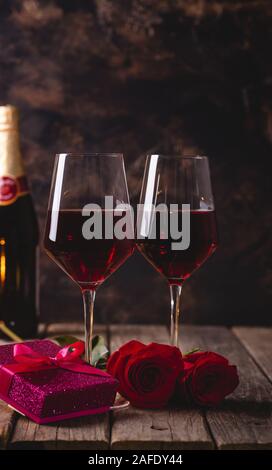 Zwei Gläser Wein mit roten Rosen und Valentinstag geschenk Box auf einem rustikalen Holztisch und Hintergrund Stockfoto