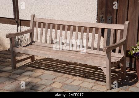 Alte Vintage Bank im Fokus mit kleinen Teil der Holz- vintage Eingangstür, Holzbank auf gepflasterten Boden Stockfoto