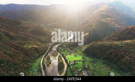 Malerischer Fluss mit Brücke verbindet kleine Dörfer im Tal zwischen forstwirtschaftlichen Hügeln mit grünen Wiesen oberen Blick. Karpaten Berge, Ukraine Schönheit Natur. Reisen, Sommerferien. Stockfoto