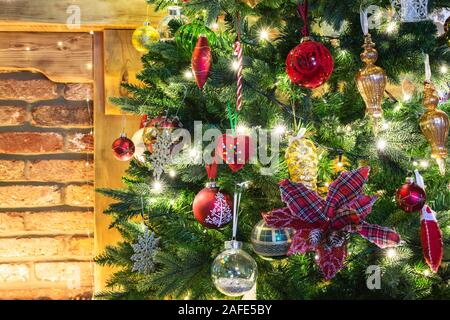 Nahaufnahme von geschmückten Weihnachtsbaum, der weihnachtsstern Blume, Christbaumkugeln, Lichterketten, selektive konzentrieren. Ziegelwand Hintergrund Stockfoto