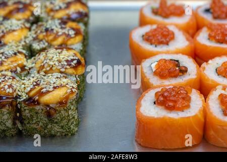 Zwei Arten von Sushi Rollen auf der Metallplatte. Mit Aal und Sesamsamen und roten Fisch und Chum salmon Kaviar. Vorderansicht. Stockfoto