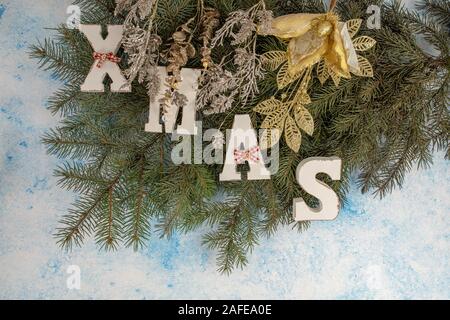 Weihnachten Hintergrund. Tannenbaum Äste mit Weihnachten Dekoration und weißen Holzmöbeln Buchstaben bilden Wort XMAS auf blauem Hintergrund. Stockfoto