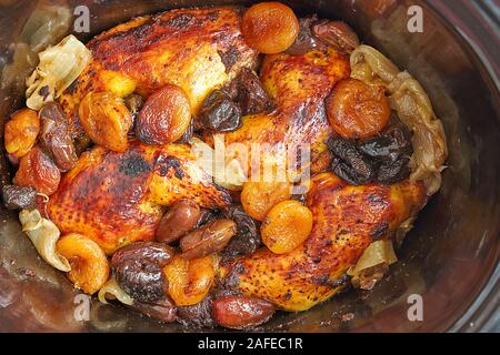 Blick von oben auf die Hähnchen mit getrockneten Aprikosen, Pflaumen und Termine in einer dunklen Tontopf auf weißem Hintergrund. Stockfoto