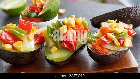 Ansicht von vorn und in der Nähe mehrerer Avocados gefüllt mit Gemüse auf einem Holzbrett, frische Kalk und eine kleine Schüssel mit Rührei und Gemüse, Stockfoto