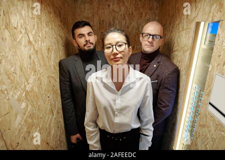 Hübsche junge elegante Frau und zwei Geschäftsleute stehen im Aufzug Stockfoto
