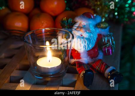 Heiligabend Hintergrund mit Tee Kerzen, Spielzeug Santa und Weihnachtsschmuck Stockfoto