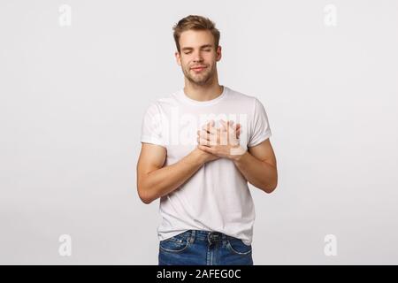 Verträumt und unbeschwerten, upbeat charmante Blonde kaukasischen Mann im weißen T-Shirt, unter Hinweis auf schöne schöne Erinnerung daran, etwas Angenehmes, Herz berühren. Stockfoto