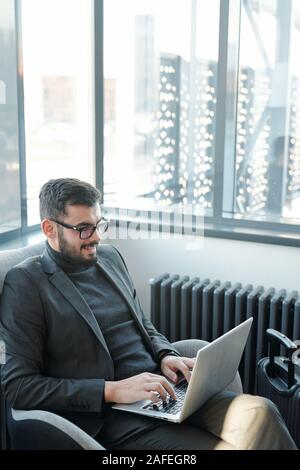 Junge erfolgreiche Geschäftsmann in Anzug im Sessel vor dem Laptop sitzen Stockfoto