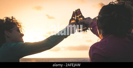 Grüße an die besten Freunde, Freunde genießen Getränke am Abend am Strand bei Sonnenuntergang. Hände, die Flaschen Bier halten. Konzept der Ferienhäuser, Stockfoto