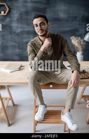 Junge schwere Geschäftsmann sitzen auf hölzernen Tisch mit seinen Füßen auf Stuhl i Stockfoto