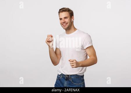 Dieser Moment, wenn lyrics Sie schlug. Fröhliche und glückliche junge Sorglos blon Kerl tanzen, schütteln Hände und lächelt erfreut, hören Musik in Wireless Stockfoto