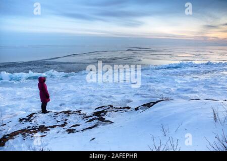 Eine Person mit einem parka Mantel einen kalten Winter Sonnenuntergang entlang der nördlichen Ufer des Lake Superior, Minnesota Stockfoto