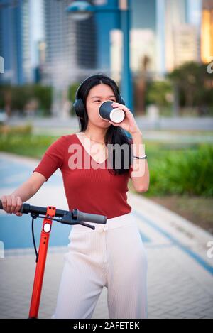 Frau mit einem Kaffee Bremse bei der Verwendung von elektrischen scooter in einer modernen Stadt Stockfoto