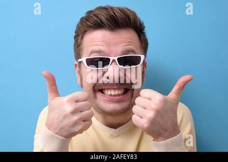 Lustige kaukasischen Mann mit Schnurrbart und retro Sonnenbrille geben einen Daumen nach oben. Positive facial menschliches Gefühl. Studio shot Stockfoto