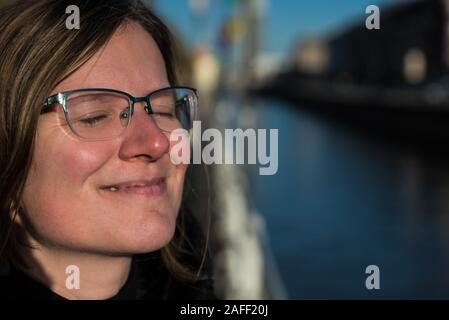 Die dreißigjährige attraktive Frau posiert am Brüsseler Kanal in der Sonne, die Augen sind geschlossen Stockfoto