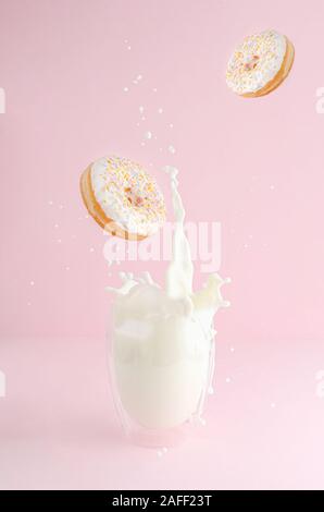 Spritzer Glas Milch und Flying Donuts mit Streuseln auf rosa Hintergrund. Kopieren Sie Platz. Levitation essen Konzept. Stockfoto
