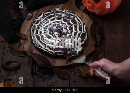 Spiderweb Kuchen von klebrigen Schokoladenkuchen kladdkaka mit einem Halloween Kürbis im Hintergrund. Eine Hand ist ein Stück Kuchen. Der Kuchen ist auf einem Stockfoto