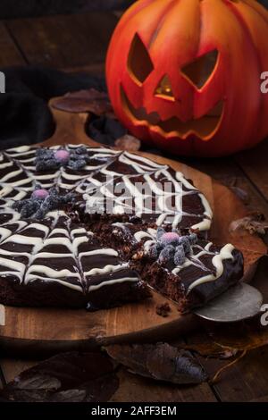 Spiderweb Kuchen von klebrigen Schokoladenkuchen kladdkaka mit einem Halloween Kürbis im Hintergrund. Der Kuchen ist auf einem Holztisch und ist wi umgeben Stockfoto