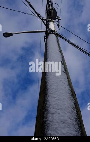 Sie suchen einen Telegrafenmast, beschichtet in Schnee, vor blauem Himmel und flauschigen weissen Wolken. Stockfoto