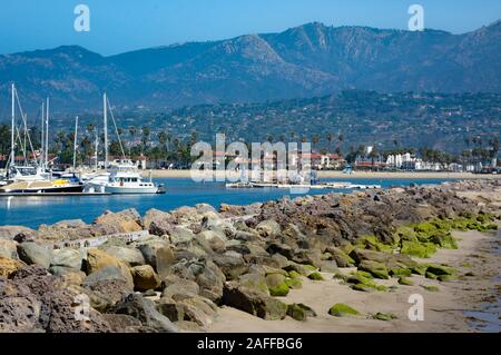 Eine weitläufige Aussicht auf den Hafen von Santa Barbara mit angedockten Segelboote und felsigen Wellenbrecher mit grünen Algen mit Santa Ynez Mountains, Santa Barbara, CA Stockfoto