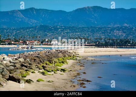 Eine weitläufige Aussicht auf den Hafen von Santa Barbara mit felsigen Wellenbrecher mit grünen Algen, eine sand Schwimmbagger und Santa Ynez Mountains, Santa Barbara, CA, USA Stockfoto