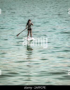 Eine isolierte einsame junge Frau Paddel ihr Stand Up Paddleboard über Open Water Stockfoto