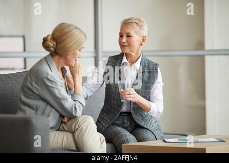 Portrait der Pflege Psychologin bietet Glas Wasser zu schreien ältere Frau, während sie während der Therapie session trösten, kopieren Raum Stockfoto