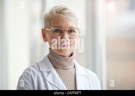 Kopf und Schultern Portrait von freundliche Ärztin lächelte Kamera, während sich gegen Fenster in Klinik, kopieren Raum Stockfoto