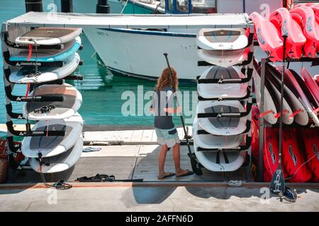 Eine junge langhaarigen Mann beaufsichtigt Stapel von Stand Up Paddle Boards für rund zusammen mit Kajaks, an der Marina in den Hafen von Santa Barbara, CA Stockfoto